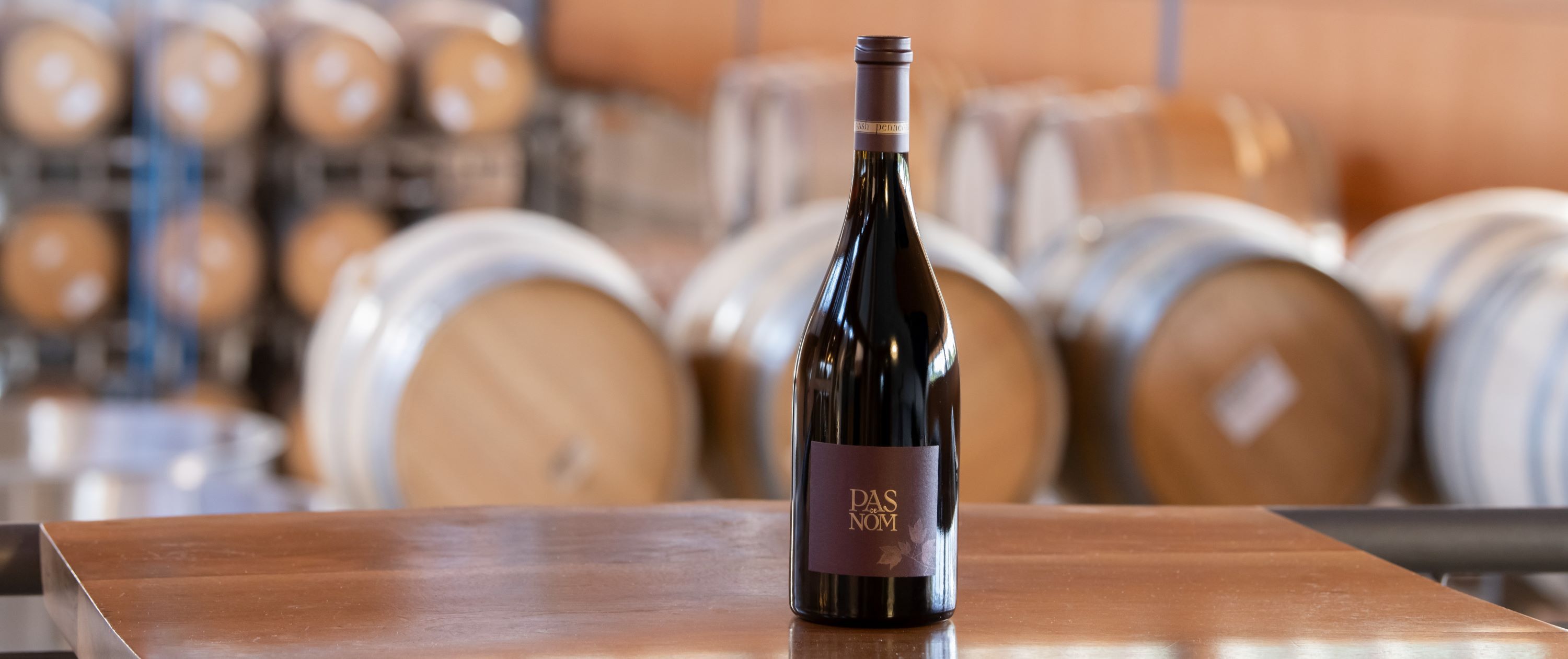 One bottle of Penner-Ash wine sitting on a table with wine barrels in the background.